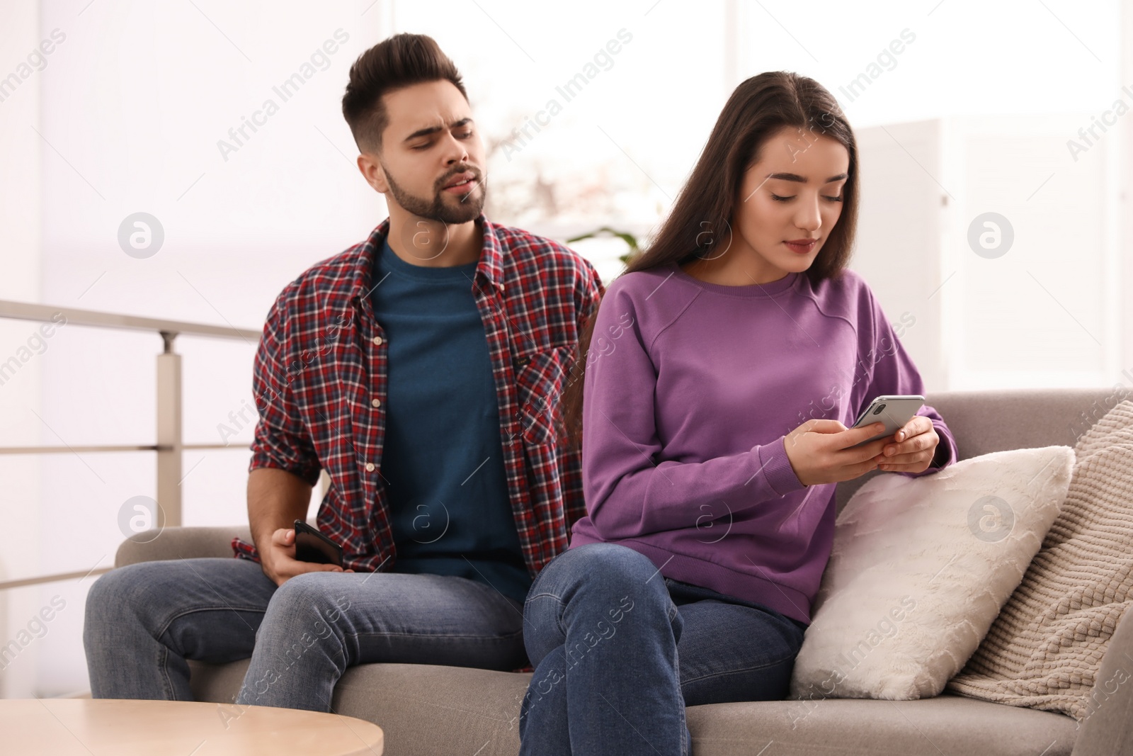 Photo of Distrustful young man peering into girlfriend's smartphone at home