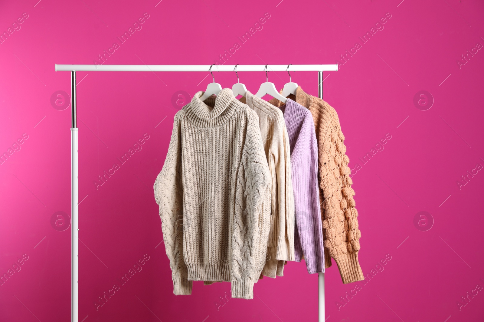 Photo of Collection of warm sweaters hanging on rack against color background