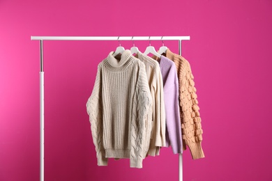 Collection of warm sweaters hanging on rack against color background