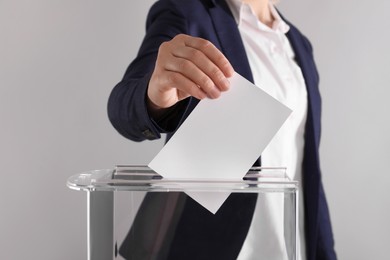 Woman putting her vote into ballot box on light grey background, closeup