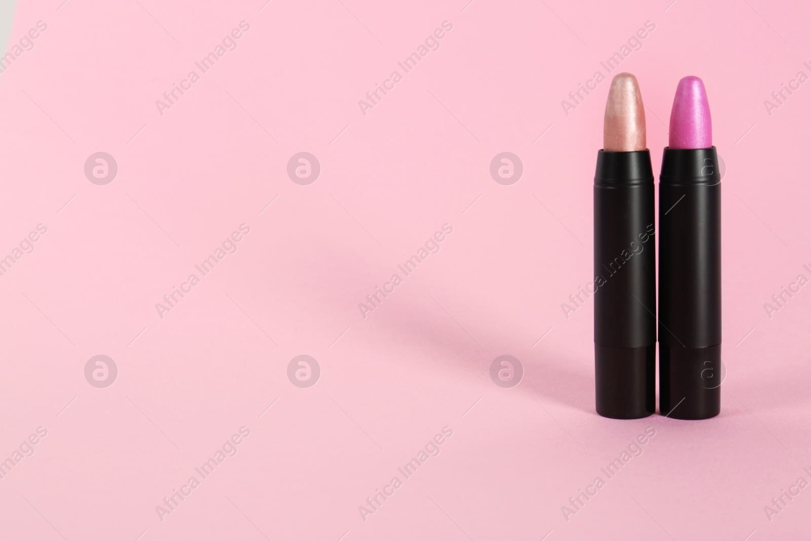 Photo of Bright lipsticks in black tubes on pink background, space for text