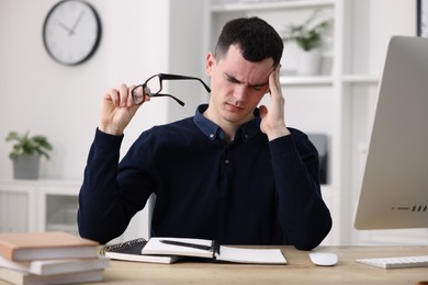 Photo of Young man with glasses suffering from headache at workplace in office