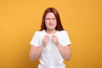 Photo of Angry woman popping bubble wrap on yellow background. Stress relief