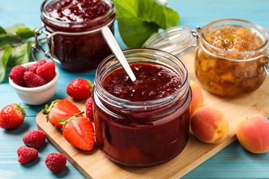 Photo of Jars with different jams and fresh fruits on light blue wooden table, closeup