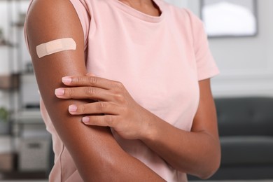 Photo of Young woman with adhesive bandage on her arm after vaccination indoors, closeup
