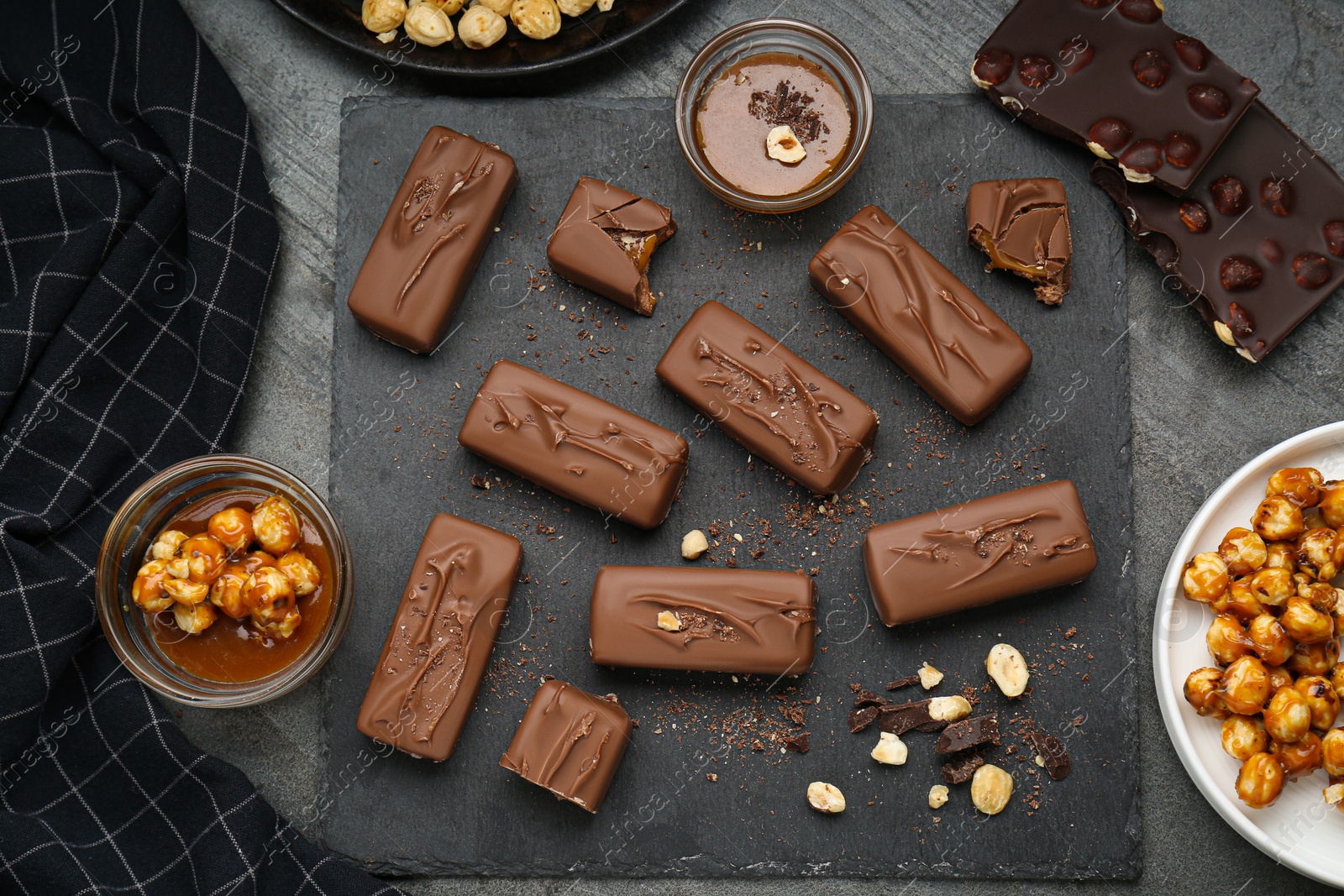 Photo of Delicious chocolate candy bars with caramel and nuts on grey table, flat lay