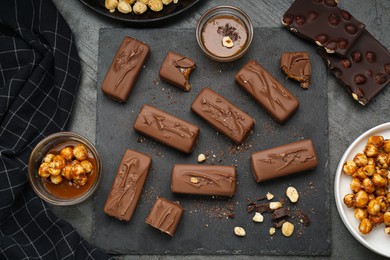 Photo of Delicious chocolate candy bars with caramel and nuts on grey table, flat lay