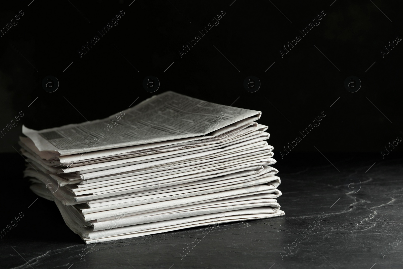 Photo of Stack of newspapers on dark stone table. Journalist's work