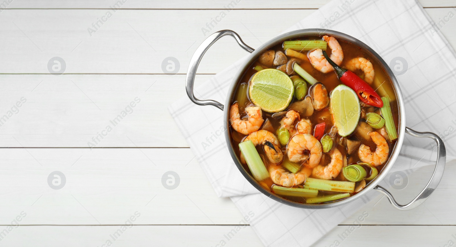 Photo of Saucepan with delicious Tom Yum soup on white wooden table, top view. Space for text