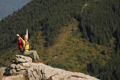Photo of Happy woman with backpack sitting on rocky peak. Mountain tourism