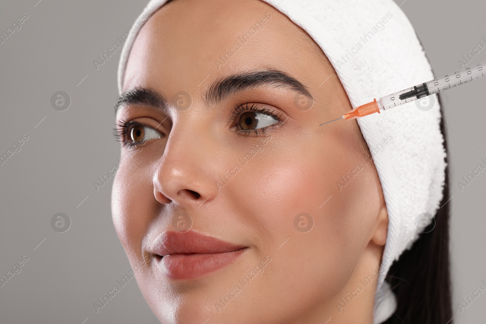 Photo of Young woman getting facial injection on light grey background, closeup. Cosmetic surgery