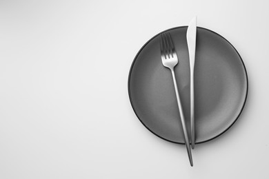 Photo of Plate, fork and knife on white background, top view. Space for text