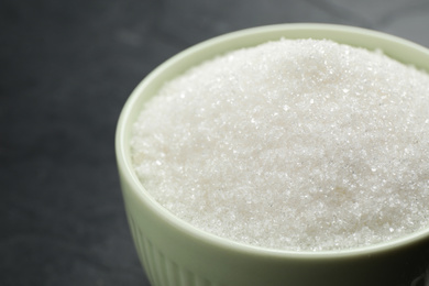 Granulated sugar in bowl on dark grey table, closeup