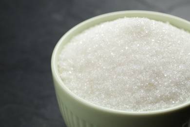 Photo of Granulated sugar in bowl on dark grey table, closeup