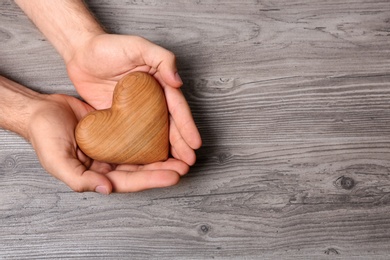 Young man holding heart on grey wooden background, top view with space for text. Donation concept