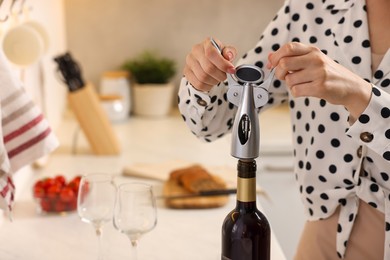 Photo of Romantic dinner. Woman opening wine bottle with corkscrew at countertop in kitchen, closeup and space for text