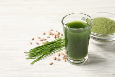 Wheat grass drink in shot glass on white wooden table, closeup