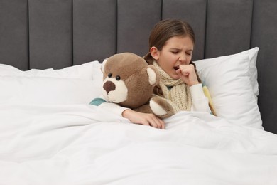 Photo of Sick girl with teddy bear coughing on bed at home