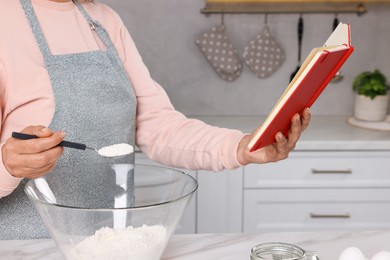 Woman with recipe book cooking in kitchen, closeup