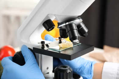 Photo of Scientist inspecting slice of lemon with microscope in laboratory, closeup. Poison detection