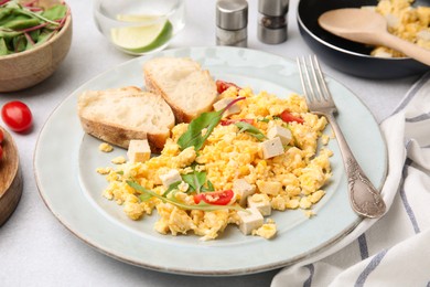 Photo of Delicious scrambled eggs with tofu and slices of baguettes served on white table, closeup