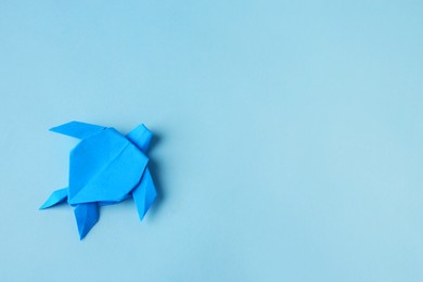Photo of Origami art. Handmade bright paper turtle on light blue background, top view with space for text