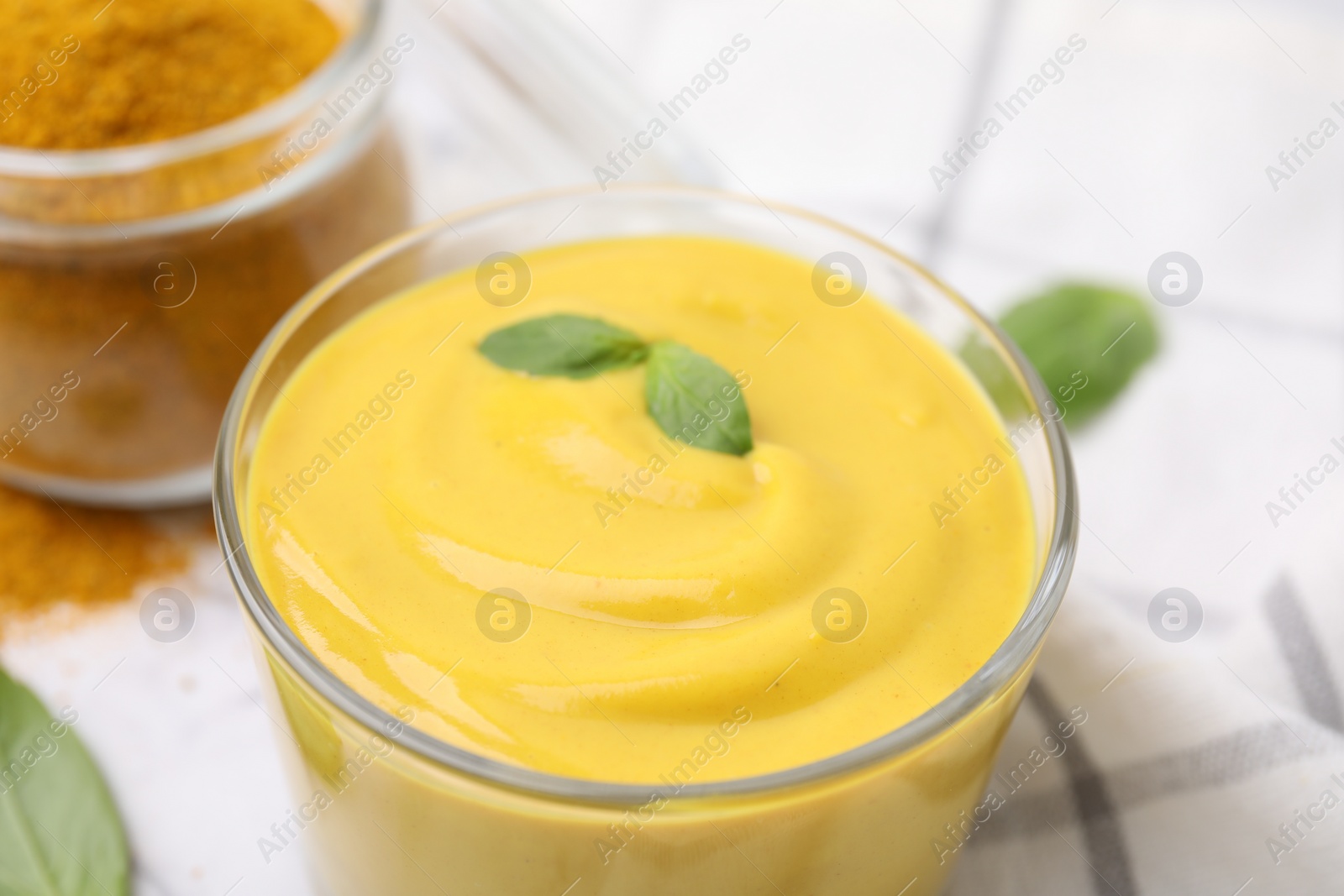 Photo of Glass with tasty curry sauce and basil leaf, closeup