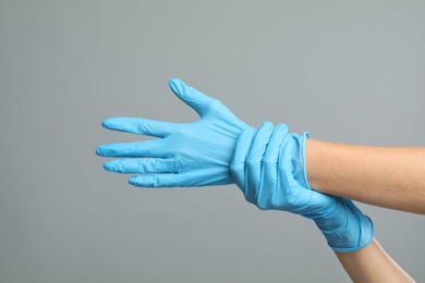 Doctor wearing medical gloves on grey background, closeup