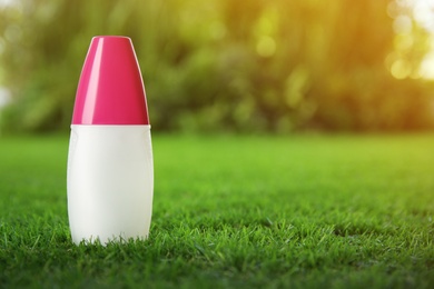 Photo of Bottle of insect repellent spray on green grass. Space for text