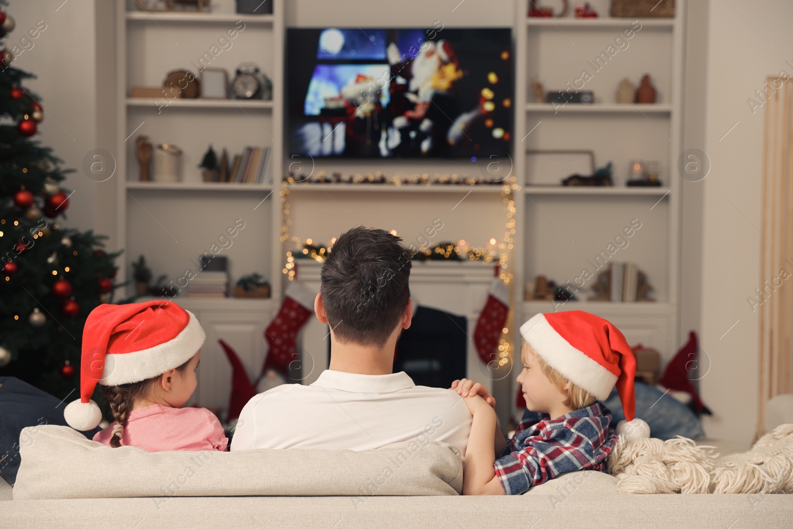 Photo of Father with his children watching TV in cosy room, back view. Christmas atmosphere