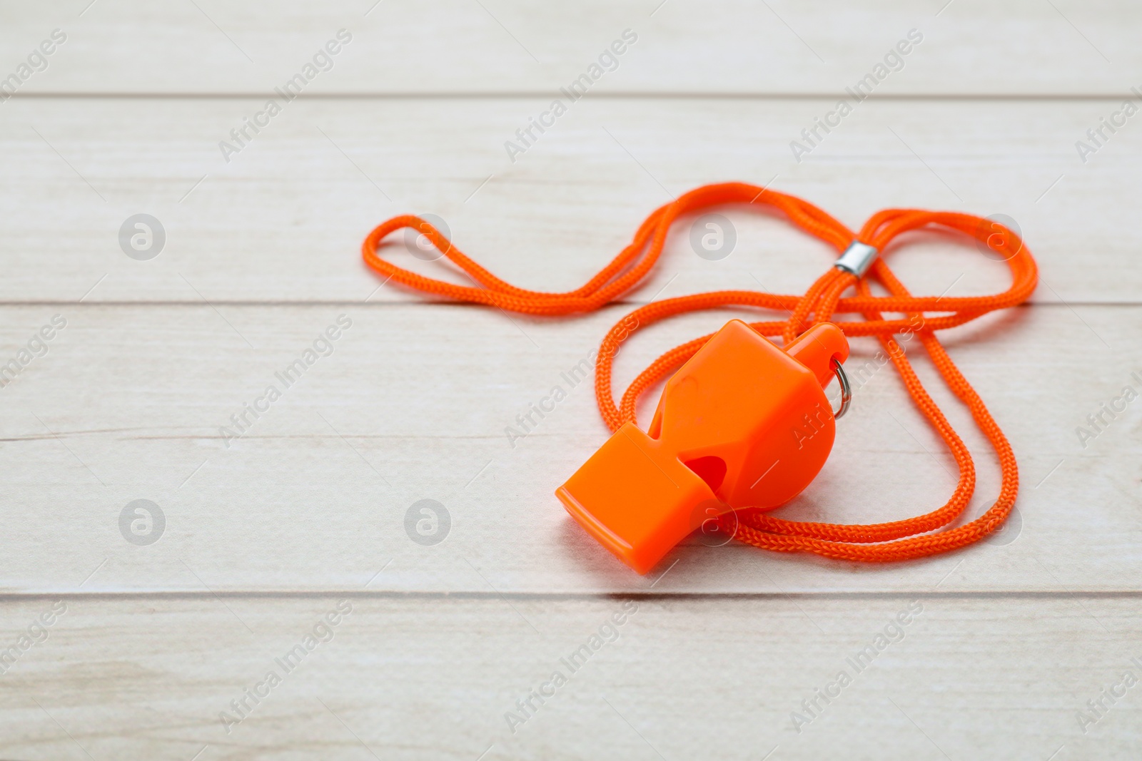 Photo of One orange whistle with cord on light wooden table. Space for text