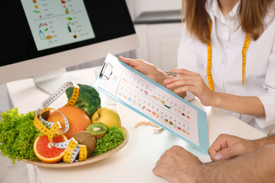 Young nutritionist consulting patient at table in clinic, closeup