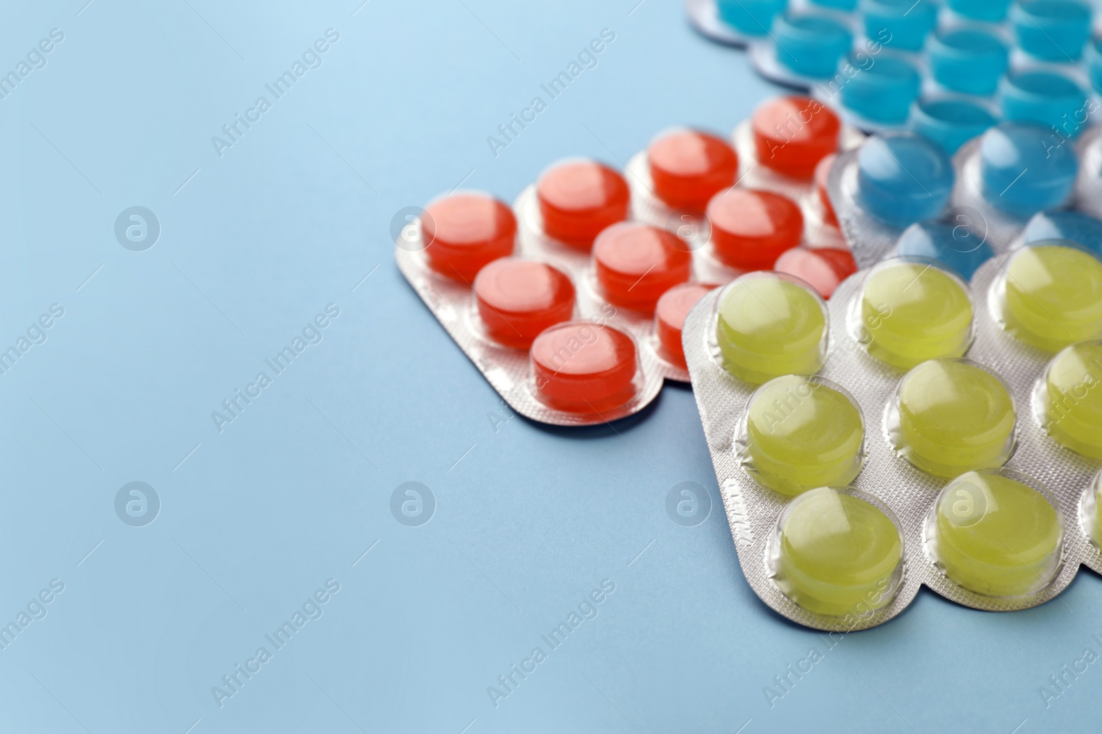 Photo of Blisters with colorful cough drops on light blue background. Space for text