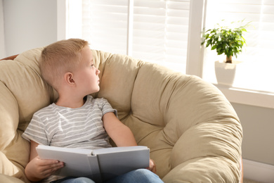 Cute little boy with book in papasan chair at home