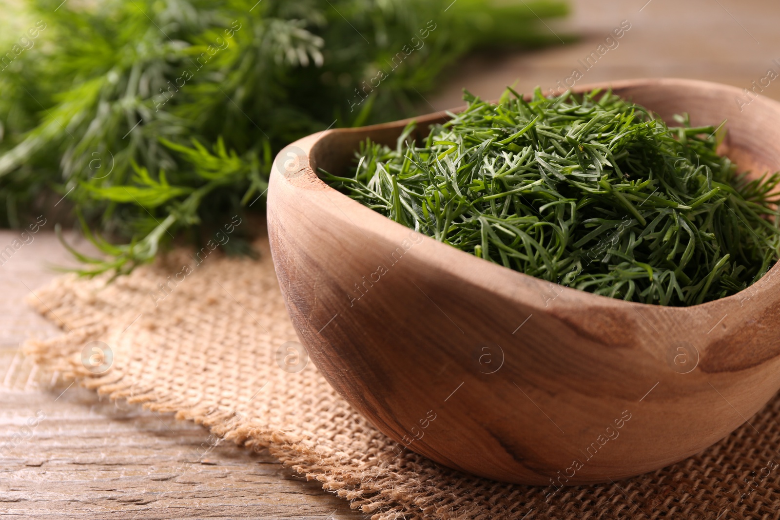 Photo of Fresh cut dill in bowl on wooden table, closeup. Space for text