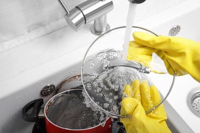 Woman washing glass lid in kitchen sink, above view