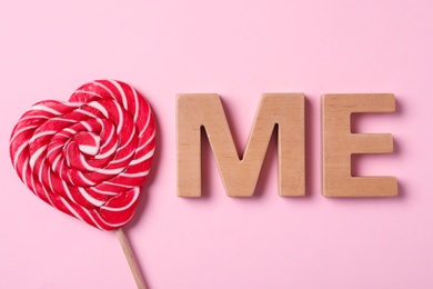 Photo of Phrase Love Me made of heart shaped lollipop and wooden letters on pink background, flat lay