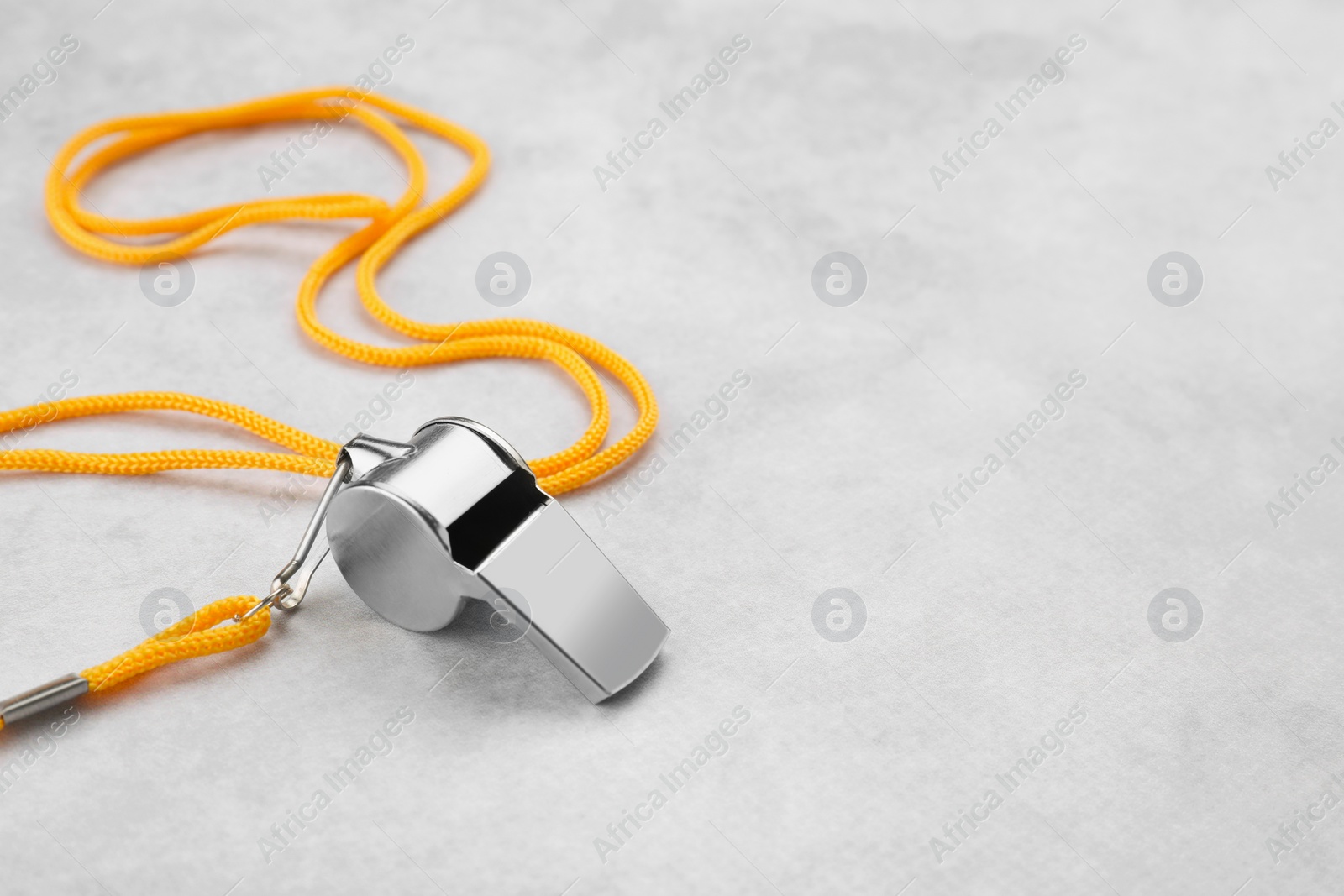 Photo of One metal whistle with cord on light grey table. Space for text