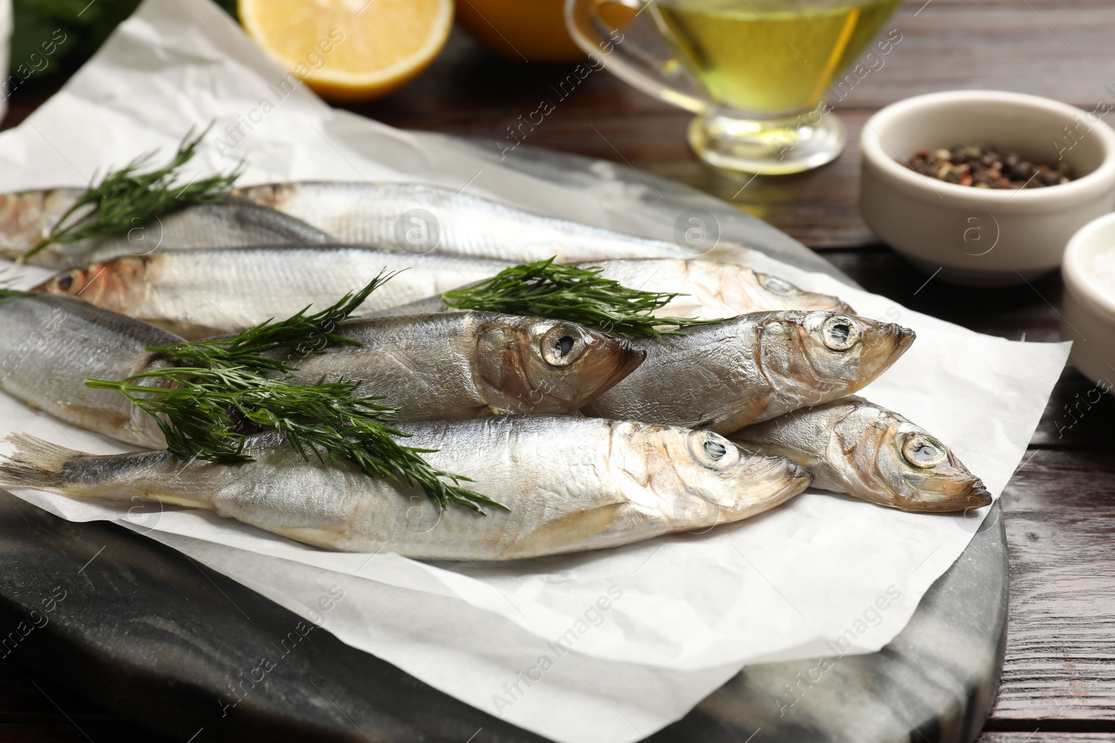 Photo of Fresh raw sprats, dill and other products on wooden table, closeup