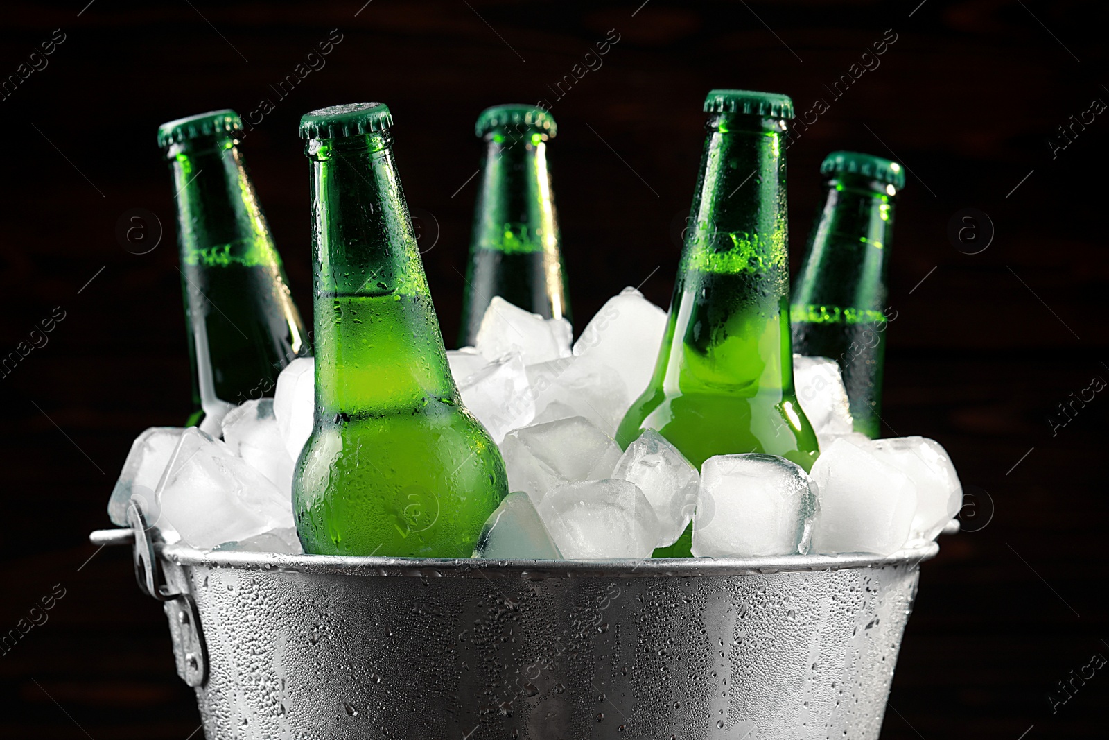 Photo of Metal bucket with bottles of beer and ice cubes on dark background, closeup