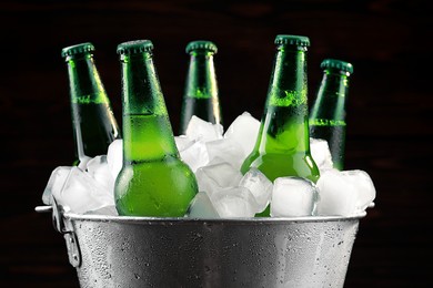 Photo of Metal bucket with bottles of beer and ice cubes on dark background, closeup