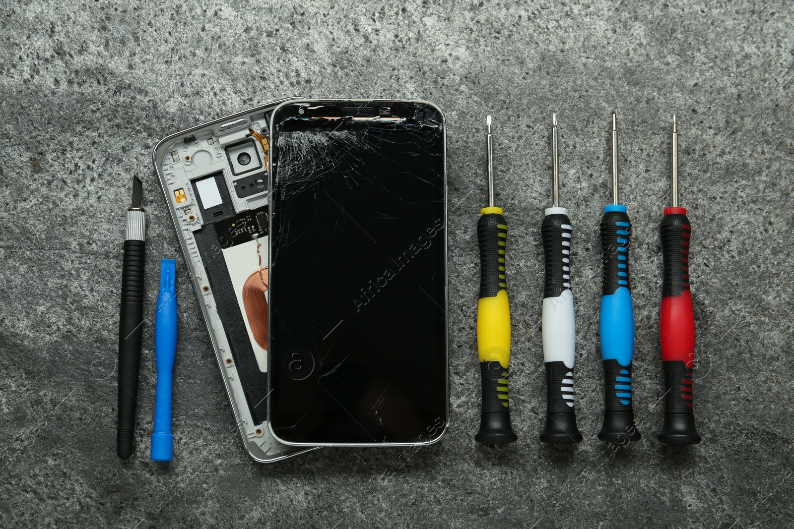 Photo of Parts of damaged smartphone and repair tool set on grey table, flat lay