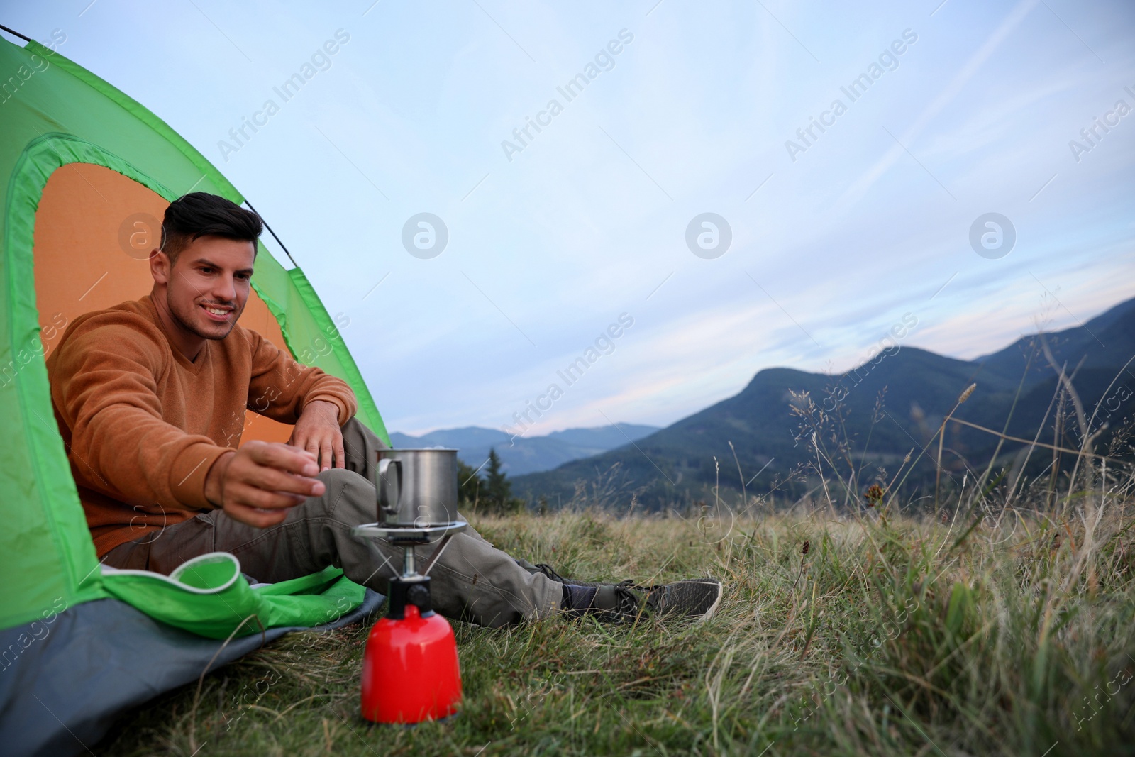 Photo of Man taking cup off stove while sitting in camping tent outdoors