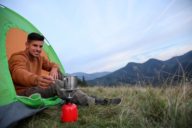 Man taking cup off stove while sitting in camping tent outdoors