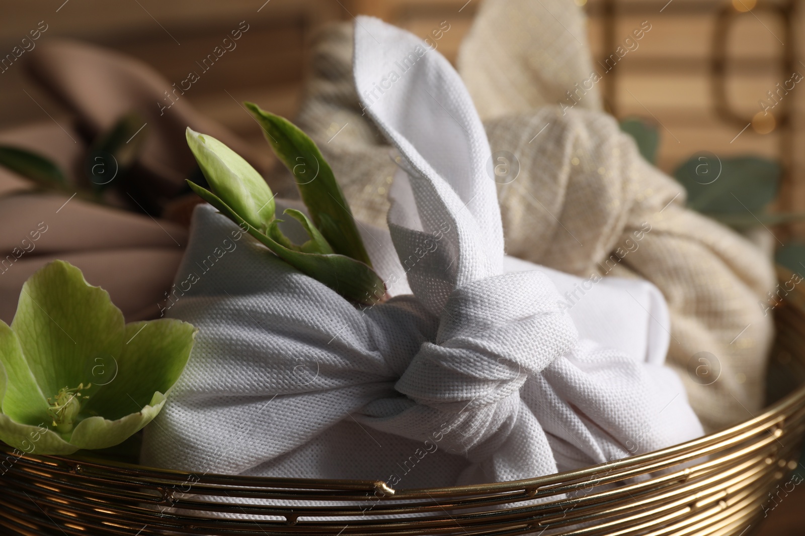 Photo of Furoshiki technique. Gifts packed in different fabrics and flowers in bowl, closeup.