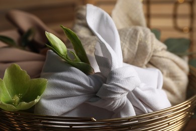Photo of Furoshiki technique. Gifts packed in different fabrics and flowers in bowl, closeup.