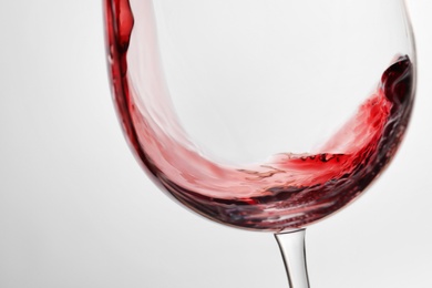 Pouring red wine into glass on light background, closeup