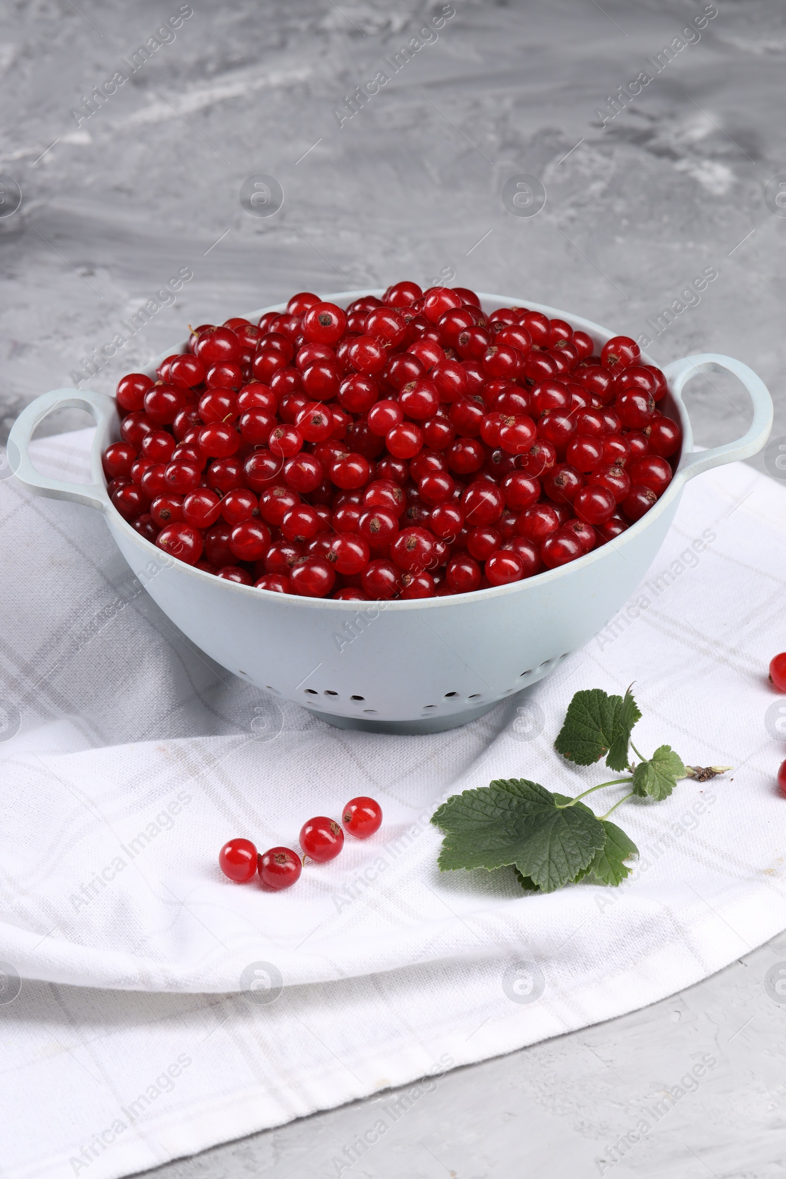 Photo of Ripe red currants in colander and leaves on grey textured table