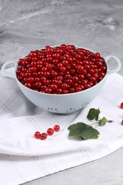 Ripe red currants in colander and leaves on grey textured table