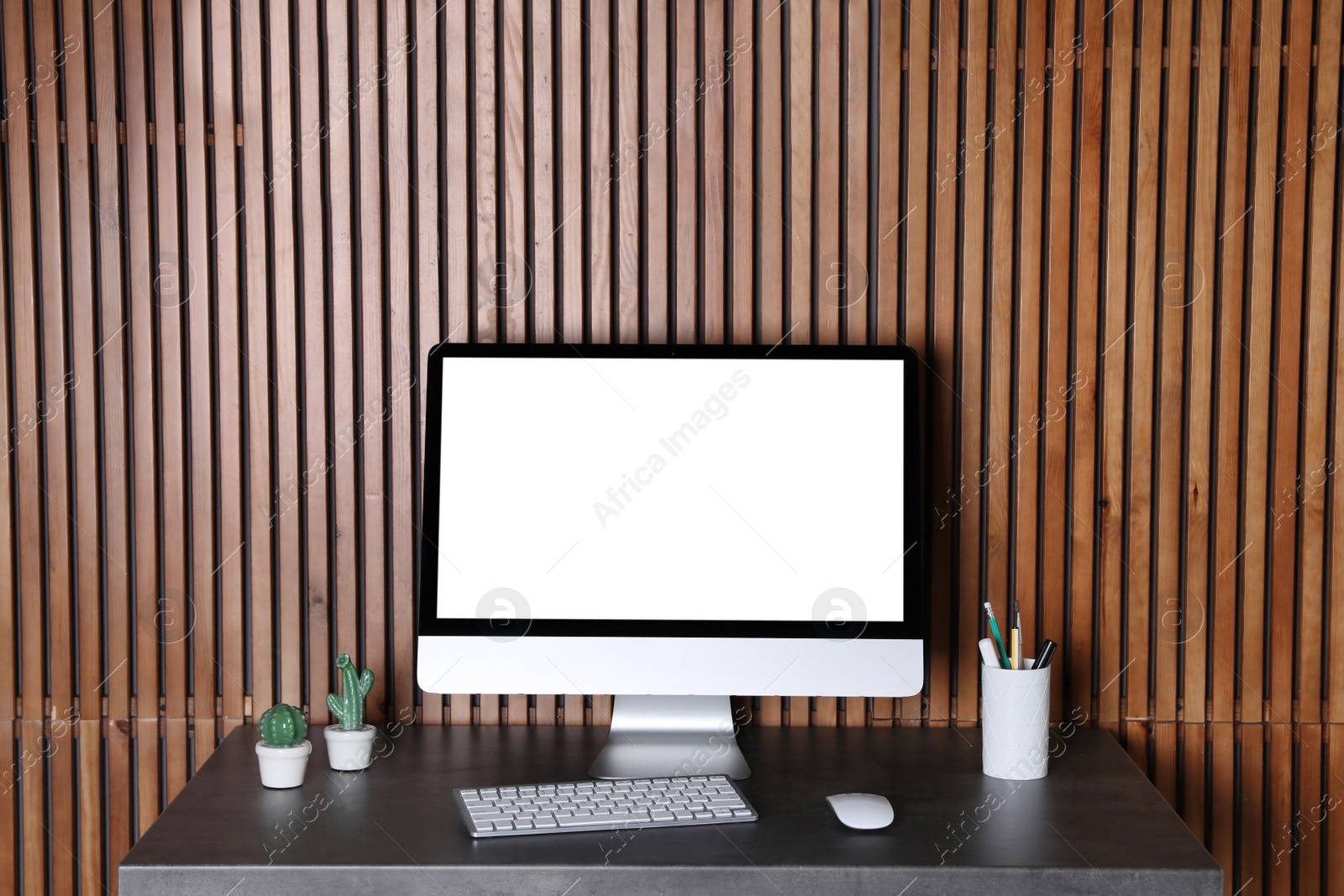 Photo of Modern computer monitor on desk against wooden wall, mock up with space for text